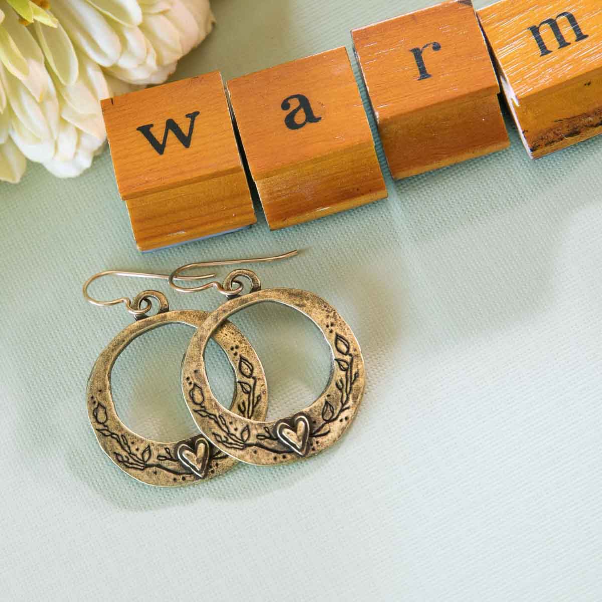 woman wearing pair of let love grow hoop earrings in bronze