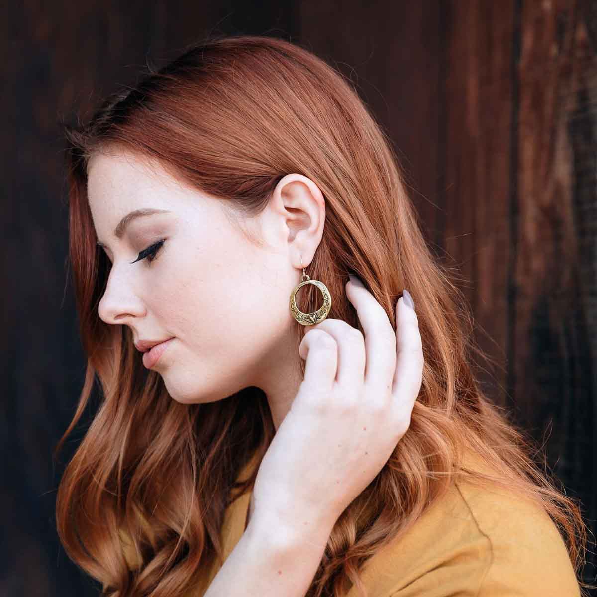 woman wearing pair of let love grow hoop earrings in bronze