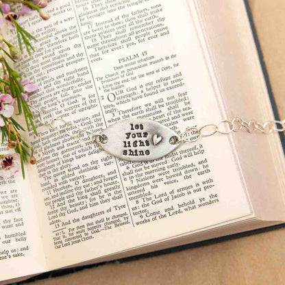 Handcrafted let your light shine pewter bracelet with a matte brushed finish on a book