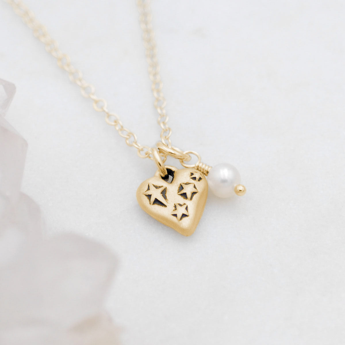 Light + Bright hearts necklace handcrafted in 10k yellow gold with a matte brushed finish and the heart charm hung next to a vintage freshwater pearl