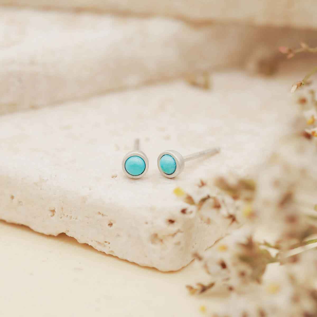 sterling silver Lighthearted Turquoise Stud Earrings on beige rock