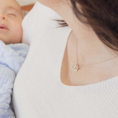 Mom wearing her Love Grows necklace handcrafted in sterling silver with the heart charm strung on sterling silver chain with her child