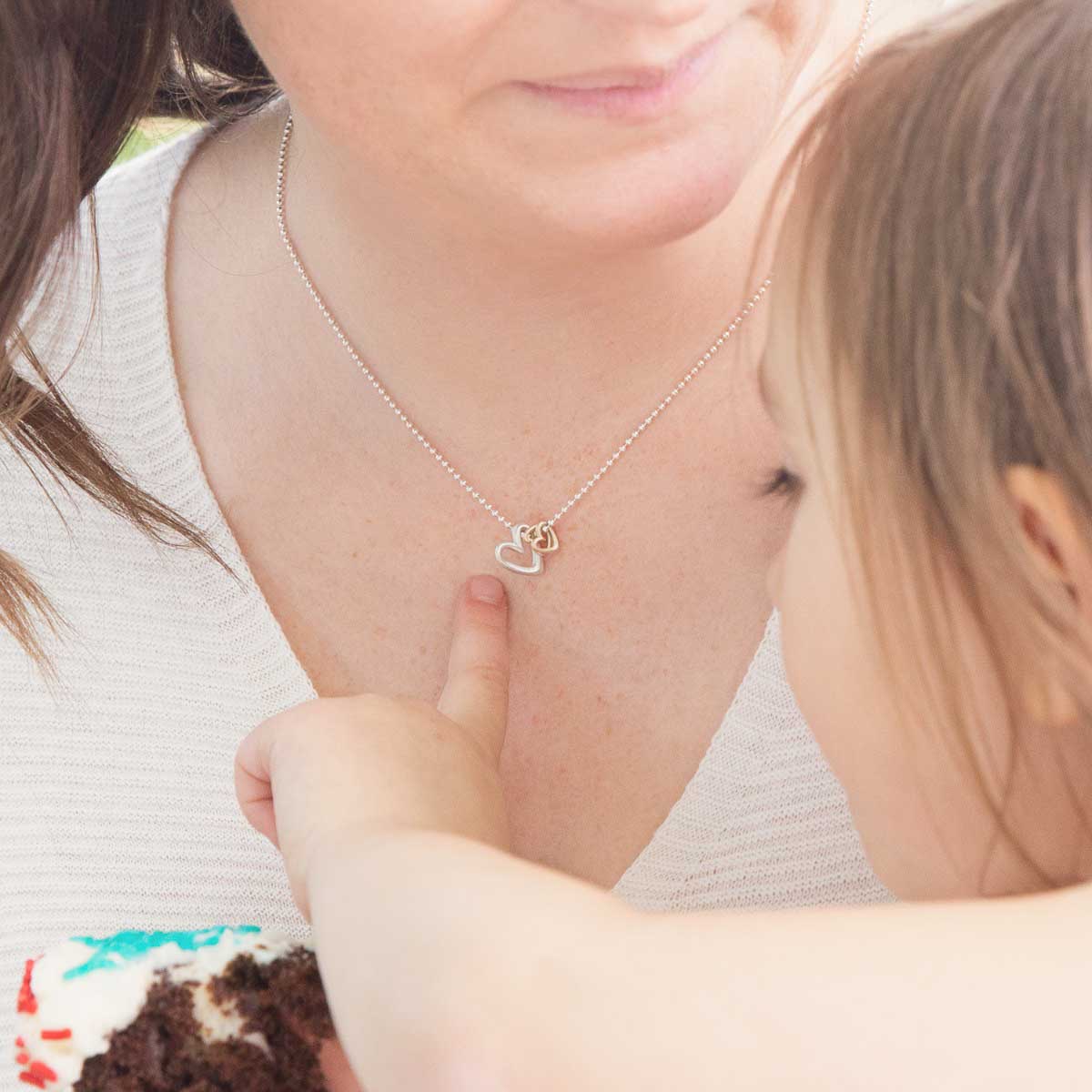 Mom wearing her Love Grows necklace handcrafted in sterling silver with the heart charm strung on sterling silver chain with her child