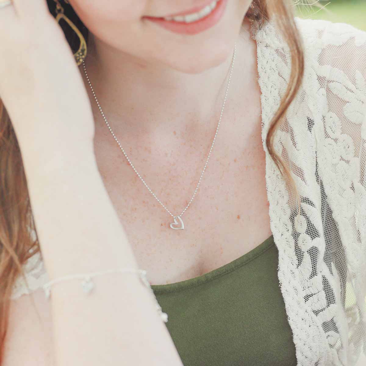 Girl wearing her Love Grows necklace handcrafted in sterling silver with the heart charm strung on sterling silver chain