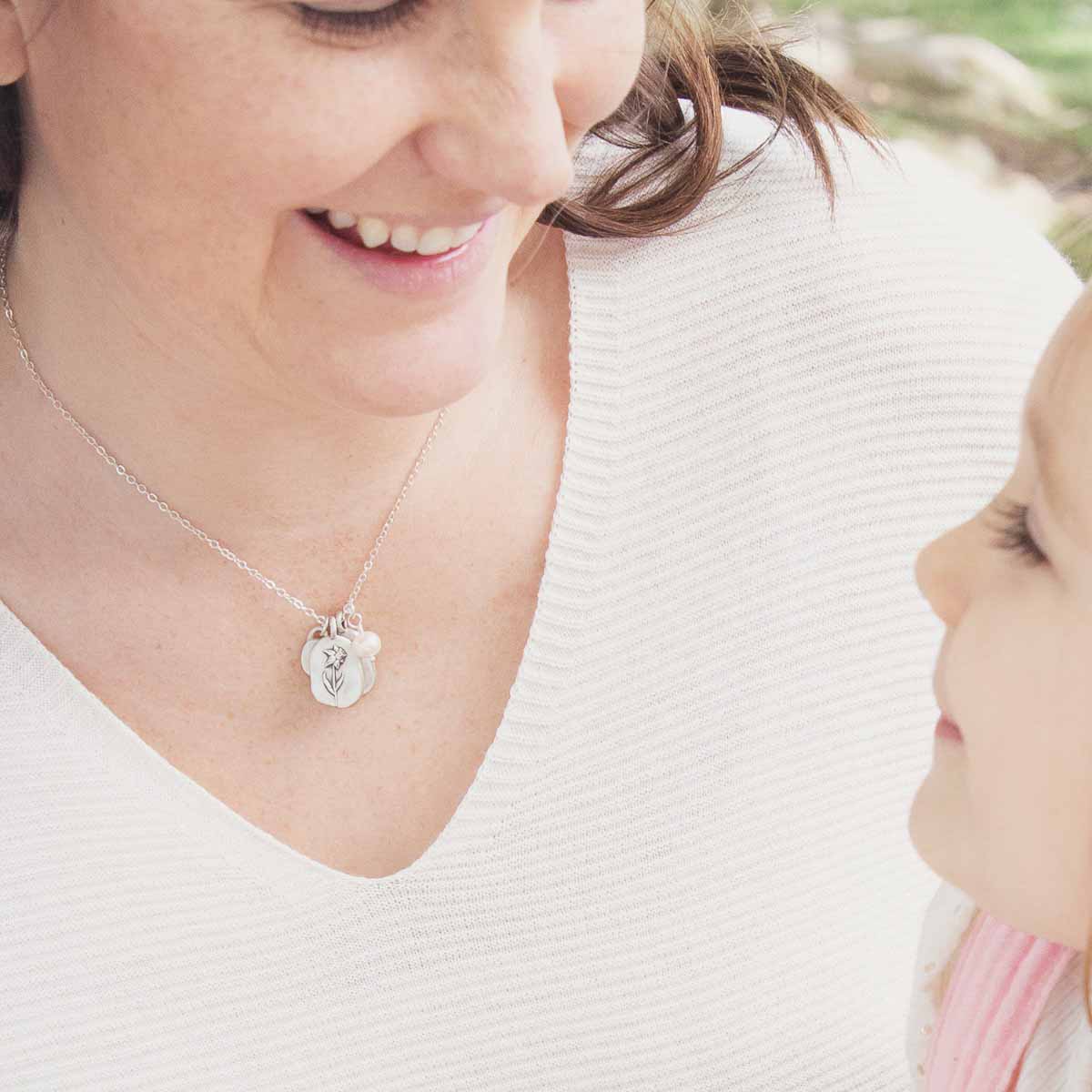 Girl wearing her March birth flower necklace handcrafted in sterling silver with a special birth month charm strung with a vintage freshwater pearl with her daughter