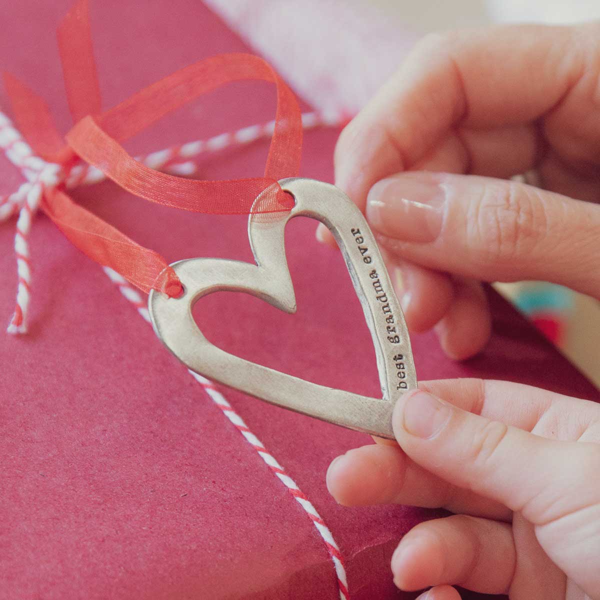 molded heart ornament handcrafted and cast in fine pewter personalized with a meaningful short phrase resting on a Christmas present