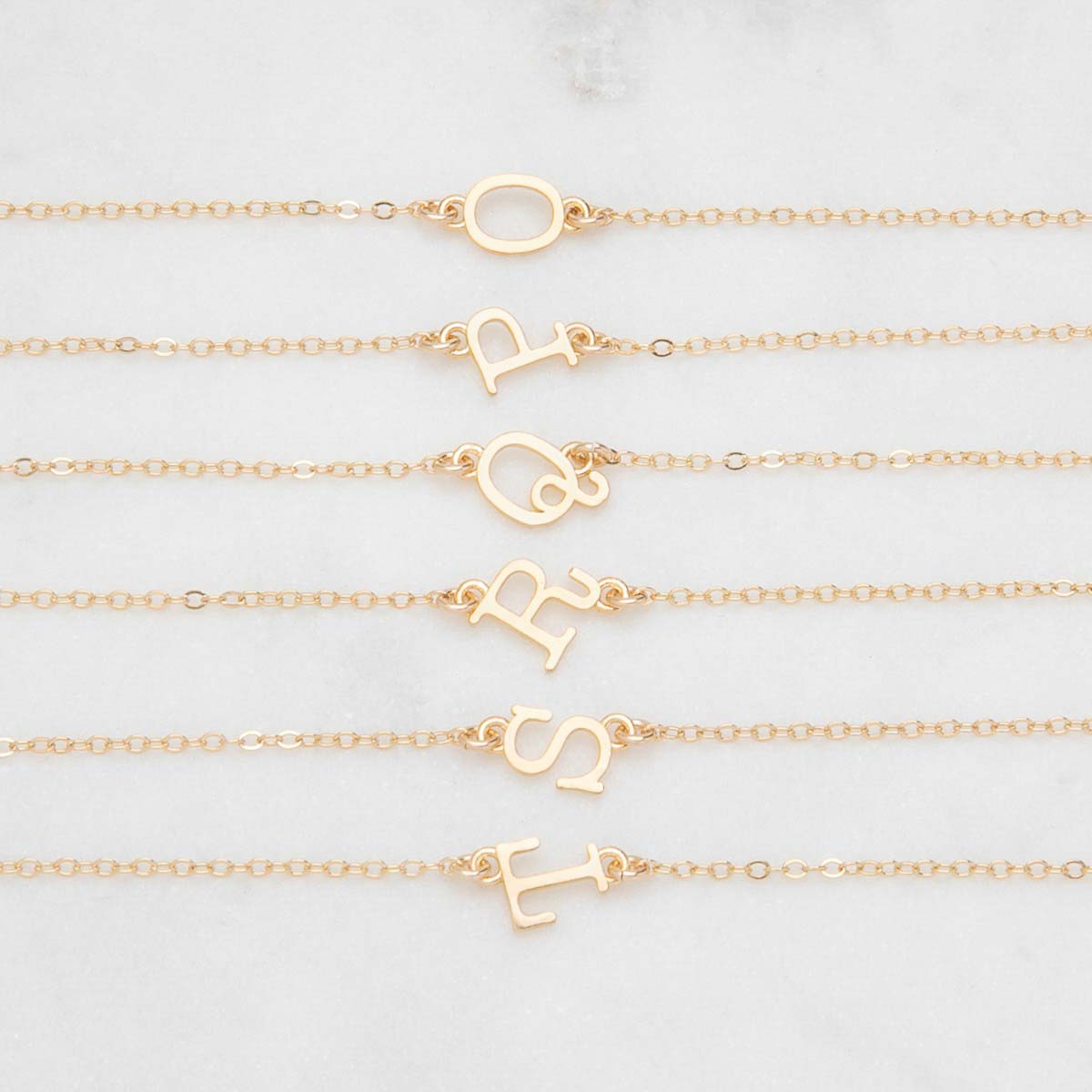 Several 10k yellow gold monogram bracelets with a satin finish going from the letters O to T