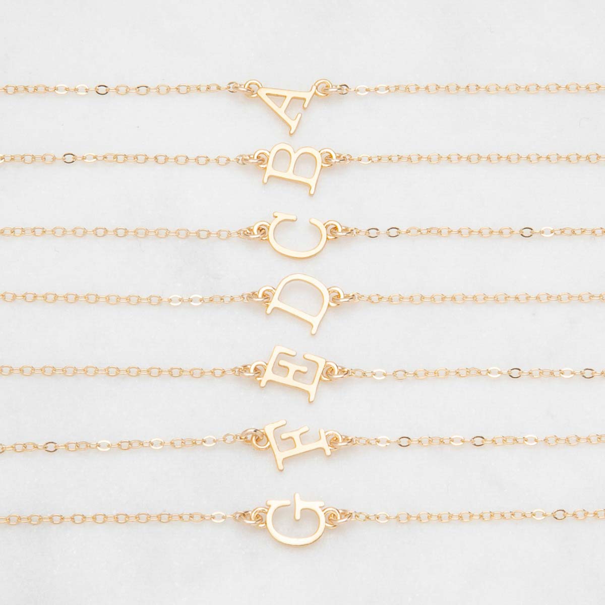 Several 14k yellow gold monogram bracelets with a satin finish going from the letters A to G