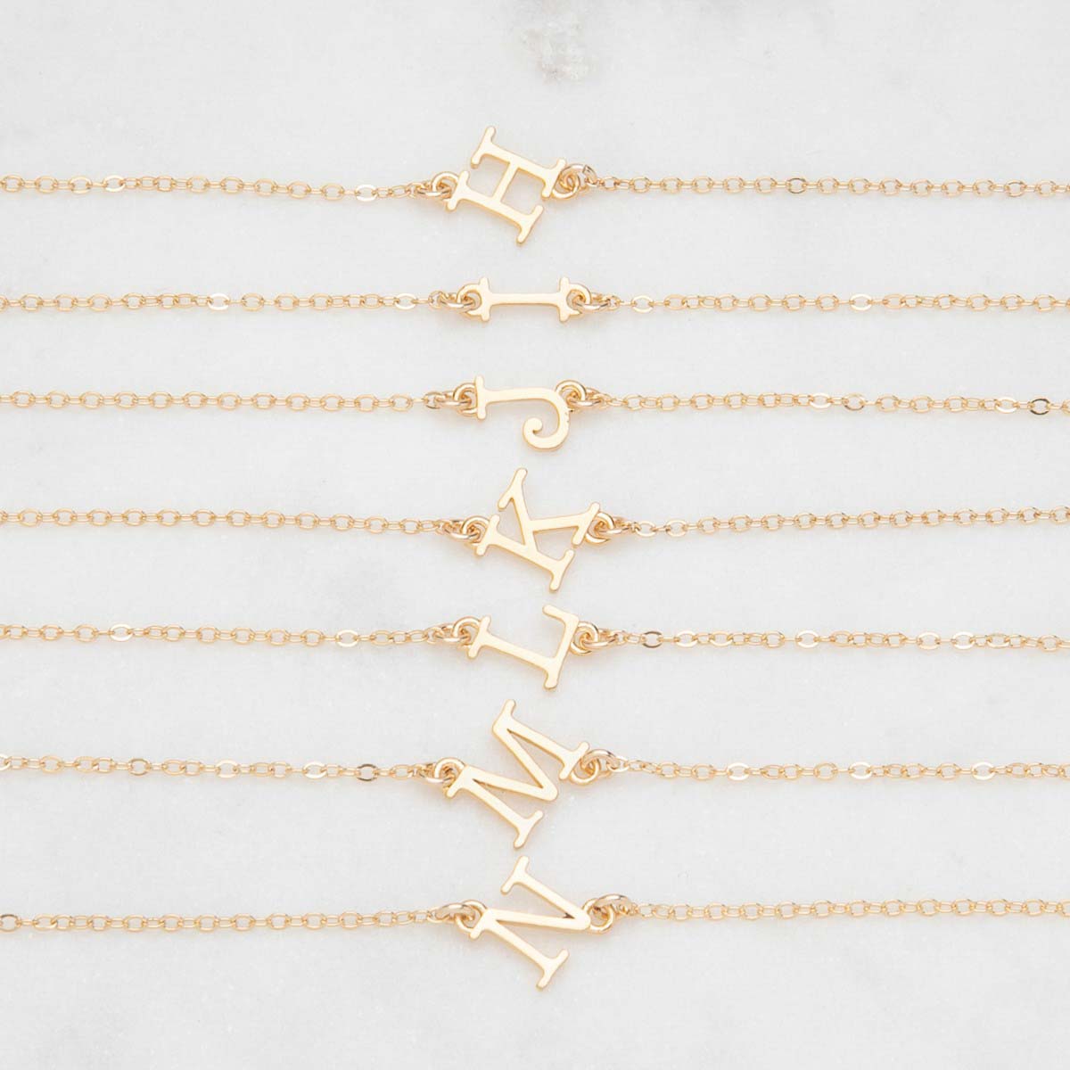 Several 14k yellow gold monogram bracelets with a satin finish going from the letters H to N