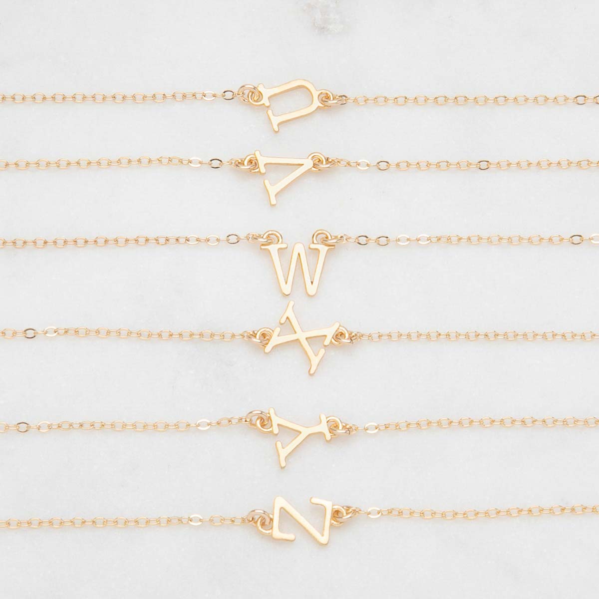 Several 14k yellow gold monogram bracelets with a satin finish going from the letters U to Z