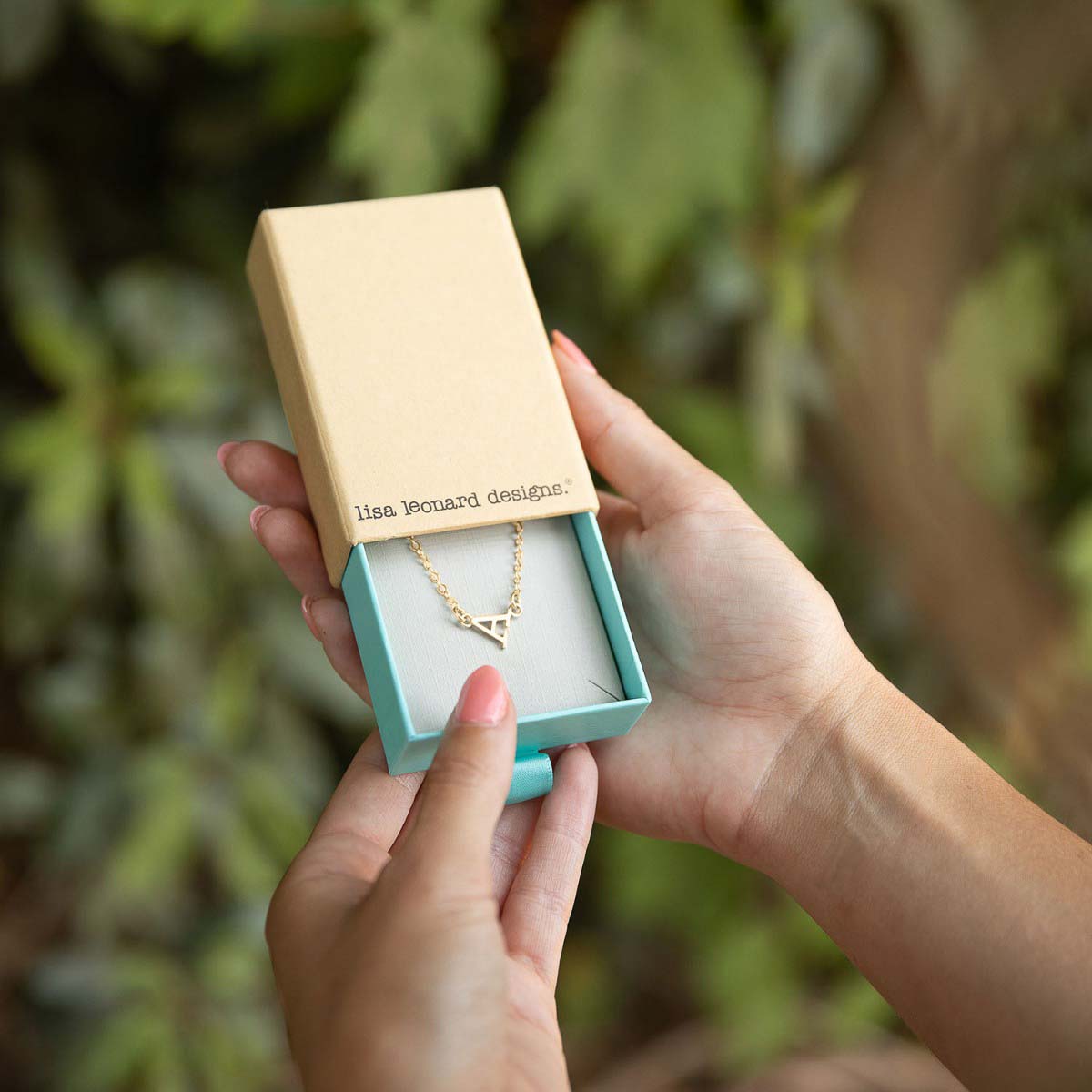 girl holding 14k yellow gold my monogram letter necklace in a lisa leonard box