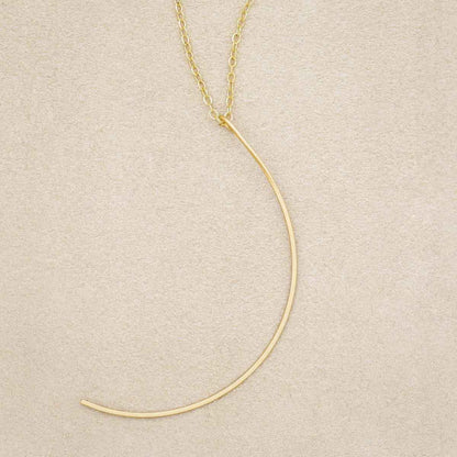 A gold filled New Moon Necklace, on beige background