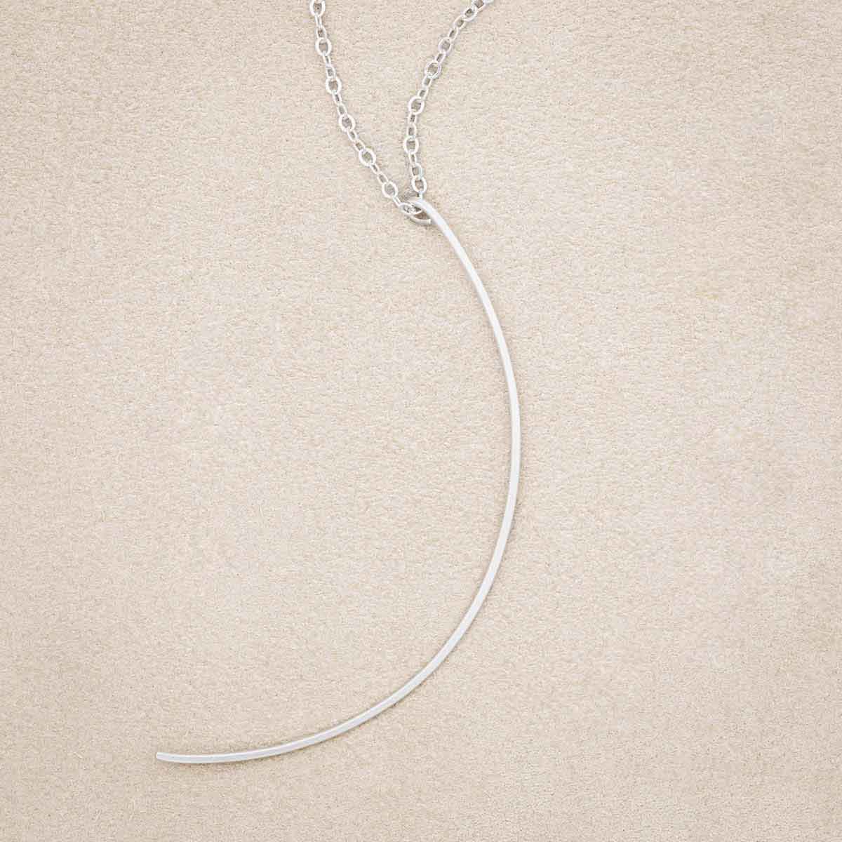 A sterling silver New Moon Necklace, on beige background