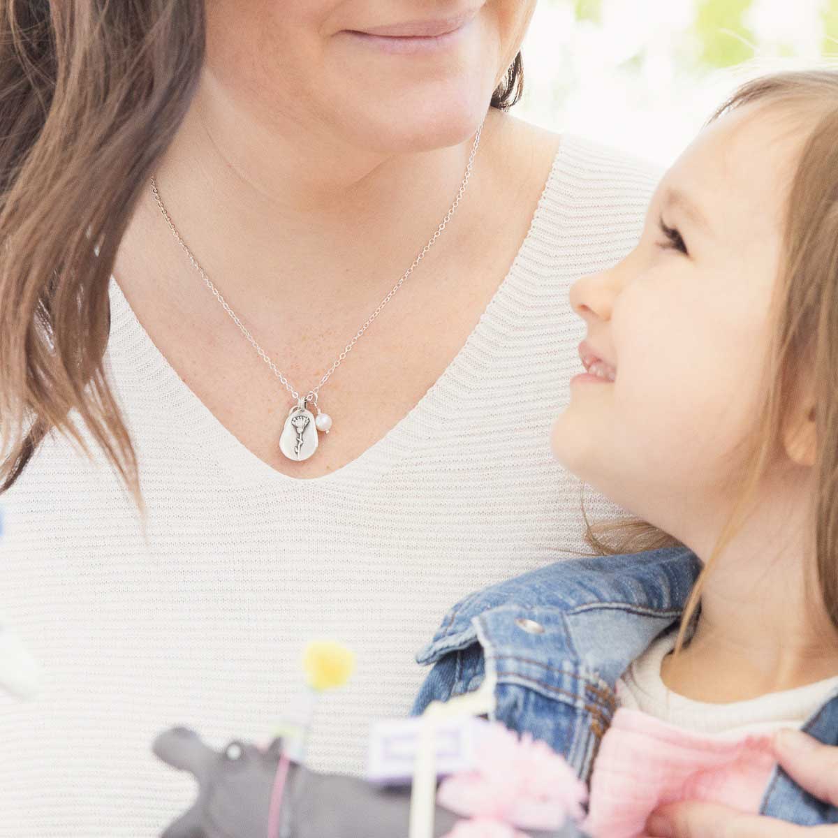 Girl wearing her October birth flower necklace handcrafted in sterling silver with a special birth month charm strung with a vintage freshwater pearl with her daughter