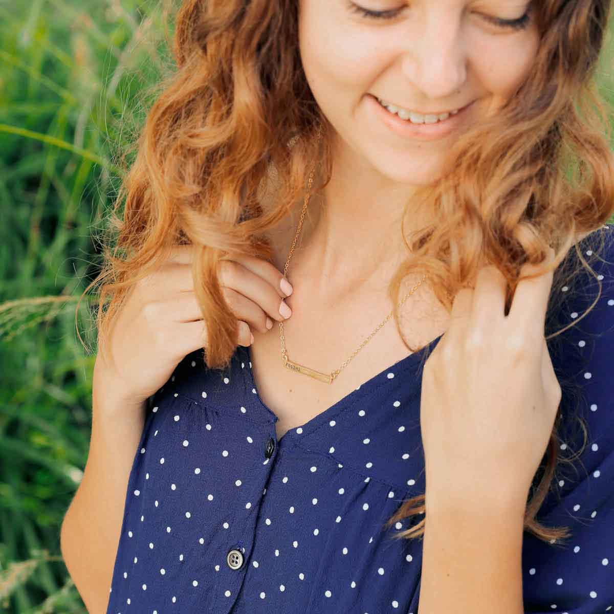 close up of girl wearing and holding a yellow gold personalized cross bar necklace