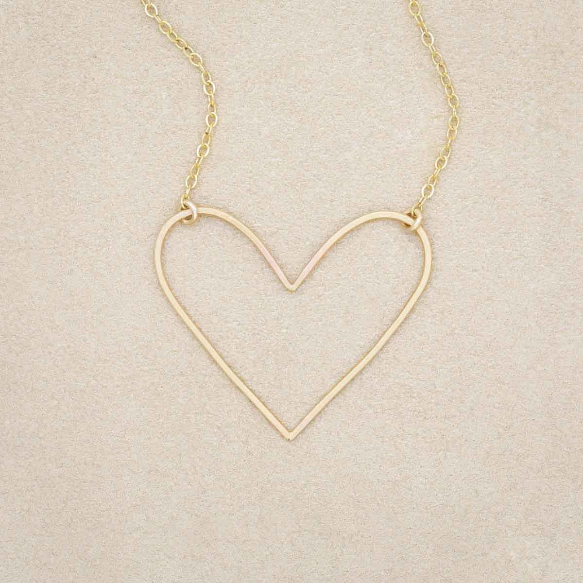 A gold filled Petite Peaceful Heart Necklace on beige background