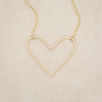 A gold filled Petite Peaceful Heart Necklace on beige background