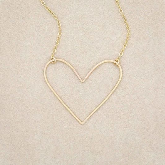 A gold filled Petite Peaceful Heart Necklace on beige background