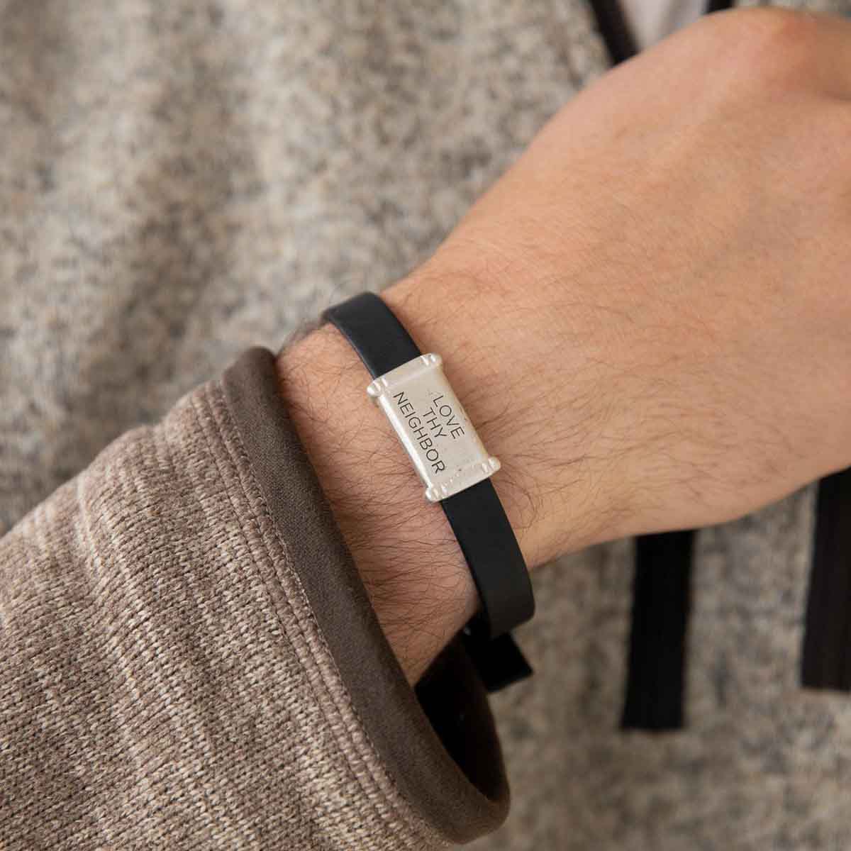 Man wearing Resolute bracelet handcrafted in black latigo leather with a sterling silver charm and button stud closure and customizable with up to 3 lines 