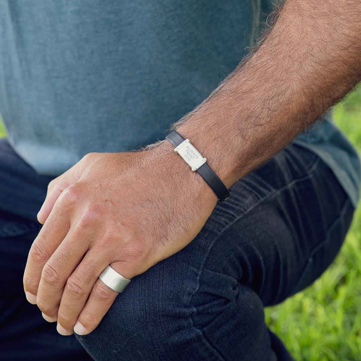 Man wearing Resolute bracelet handcrafted in black latigo leather with a sterling silver charm and button stud closure and customizable with up to 3 lines 