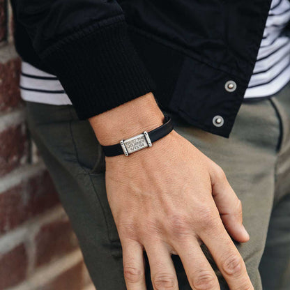 Man wearing Resolute bracelet handcrafted in black latigo leather with a sterling silver charm and button stud closure and customizable with up to 3 lines 