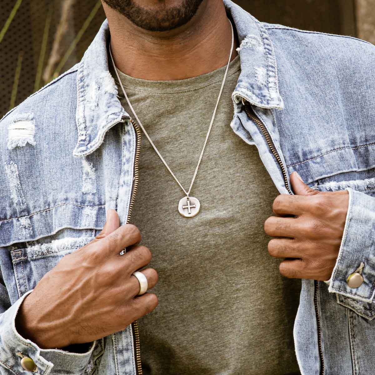 Man wearing Roman Cross Coin necklace handcrafted in sterling silver strung on sterling silver curb chain along with other sterling silver jewelry