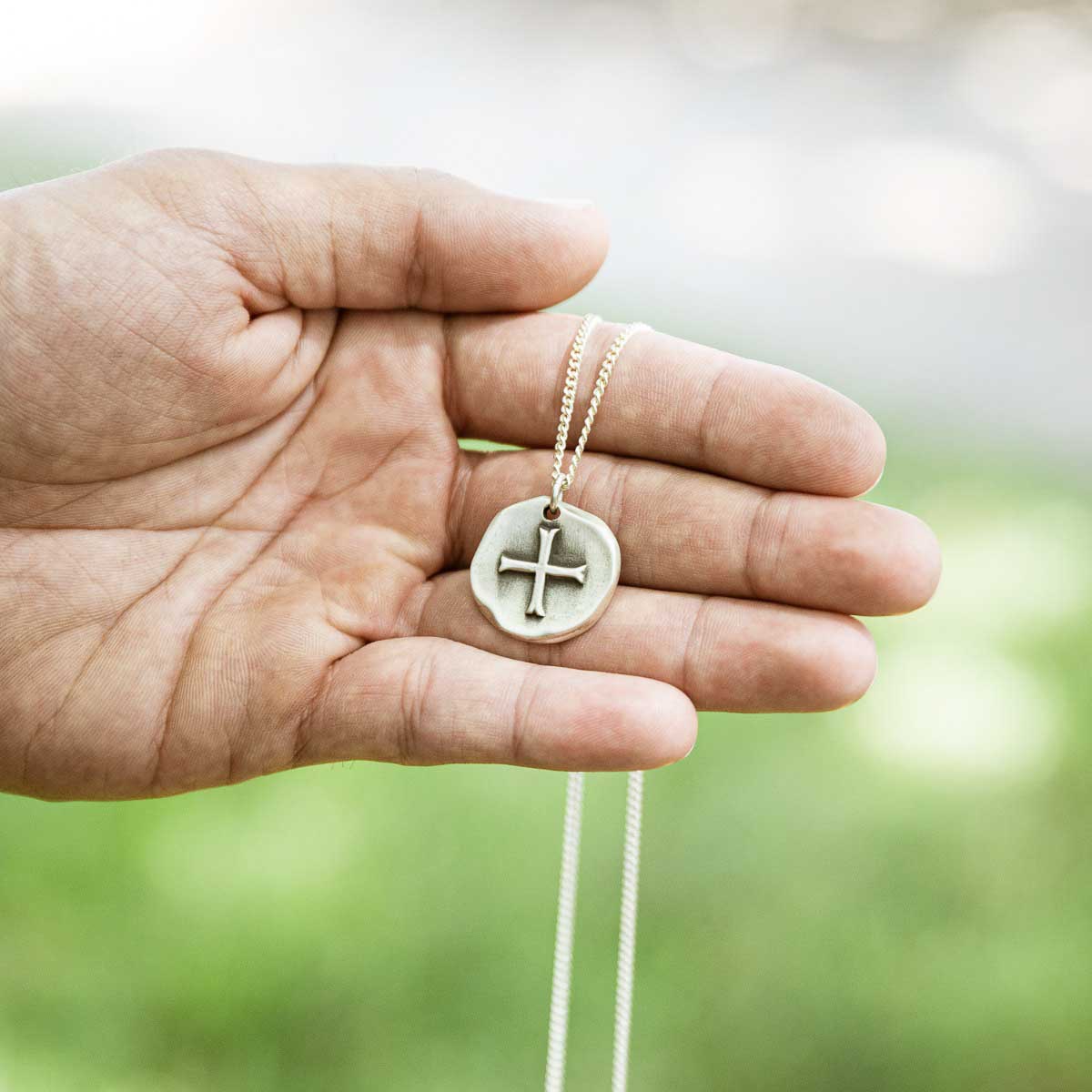 Roman Cross Coin necklace handcrafted in sterling silver strung on sterling silver curb chain being displayed