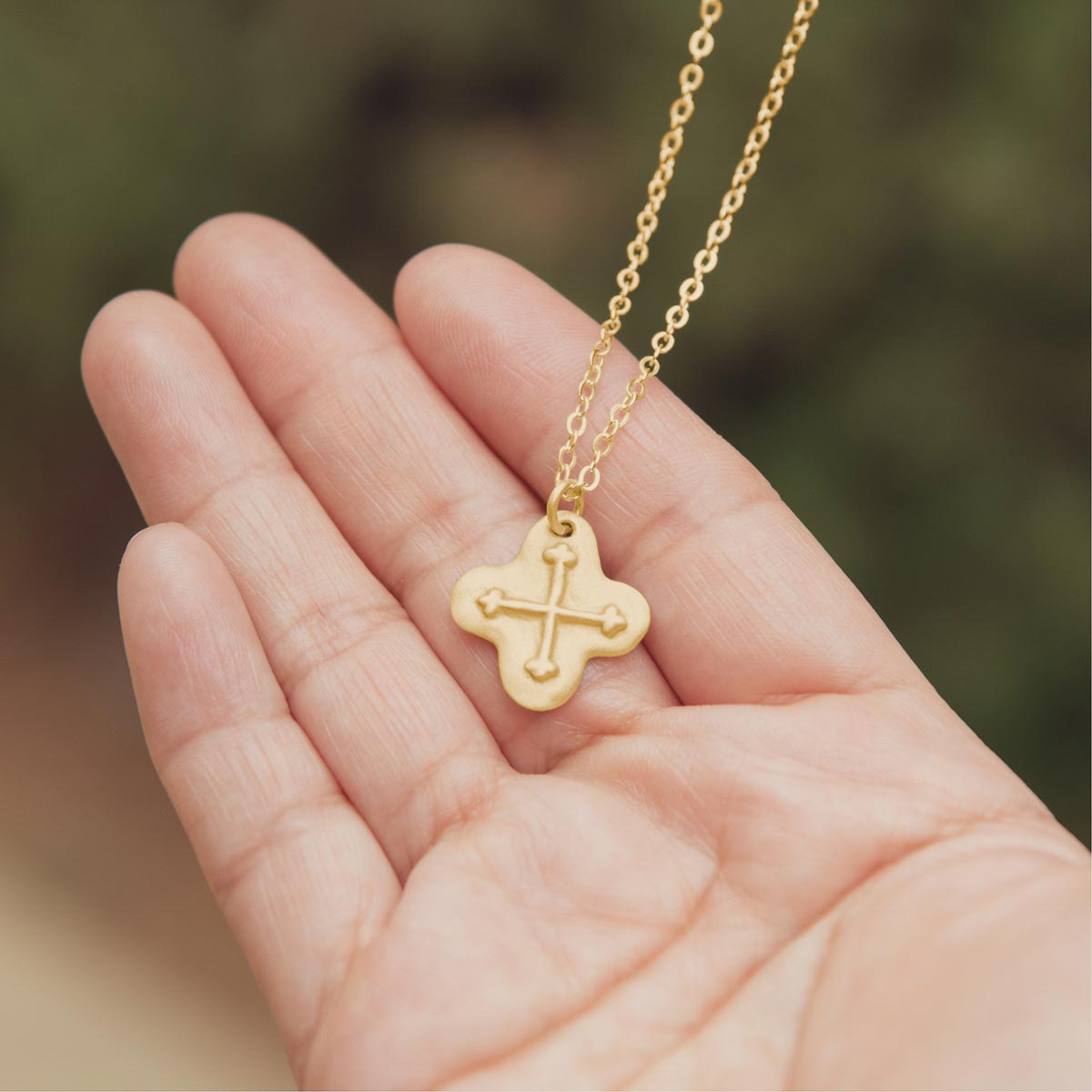 hand holding 14k yellow gold shining light cross necklace