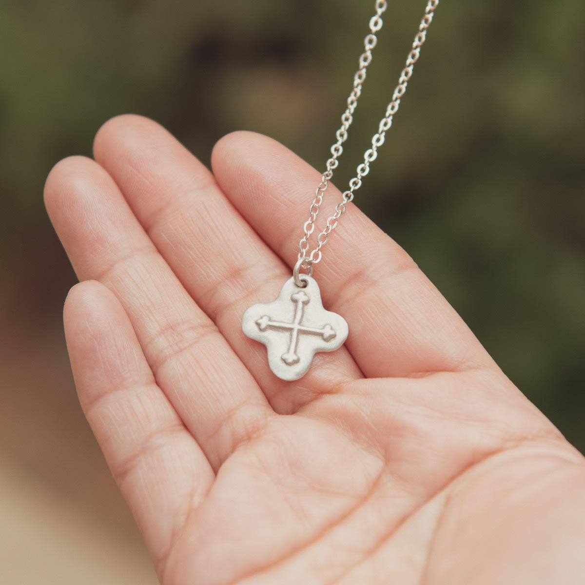 hand holding sterling silver shining light cross necklace