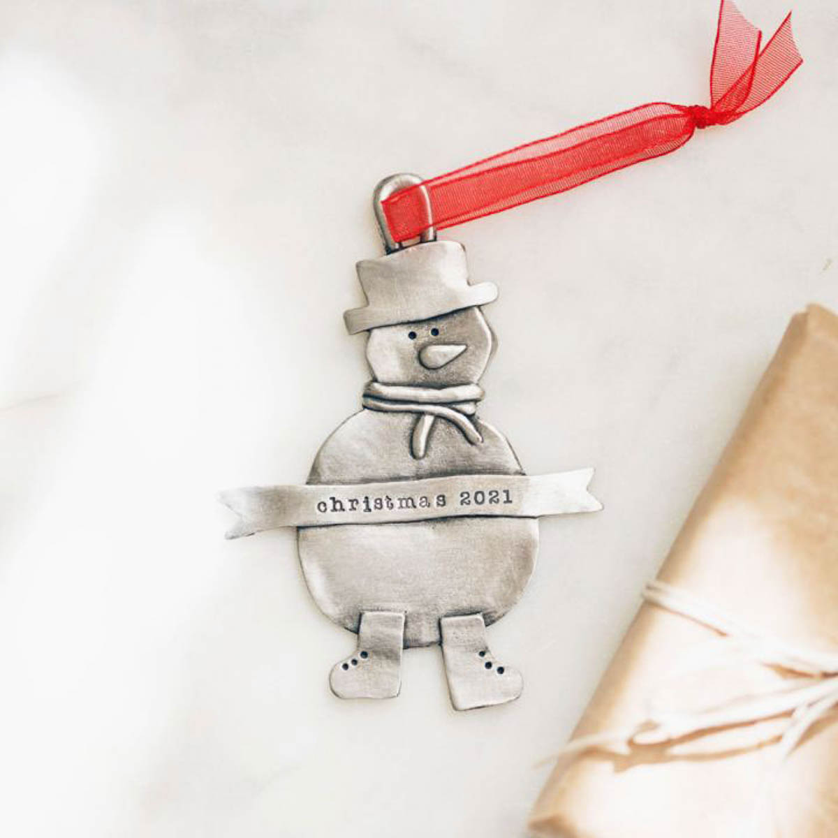 Snowman ornament hand-molded and cast in pewter hung from a sheer red ribbon and personalized with a phrase