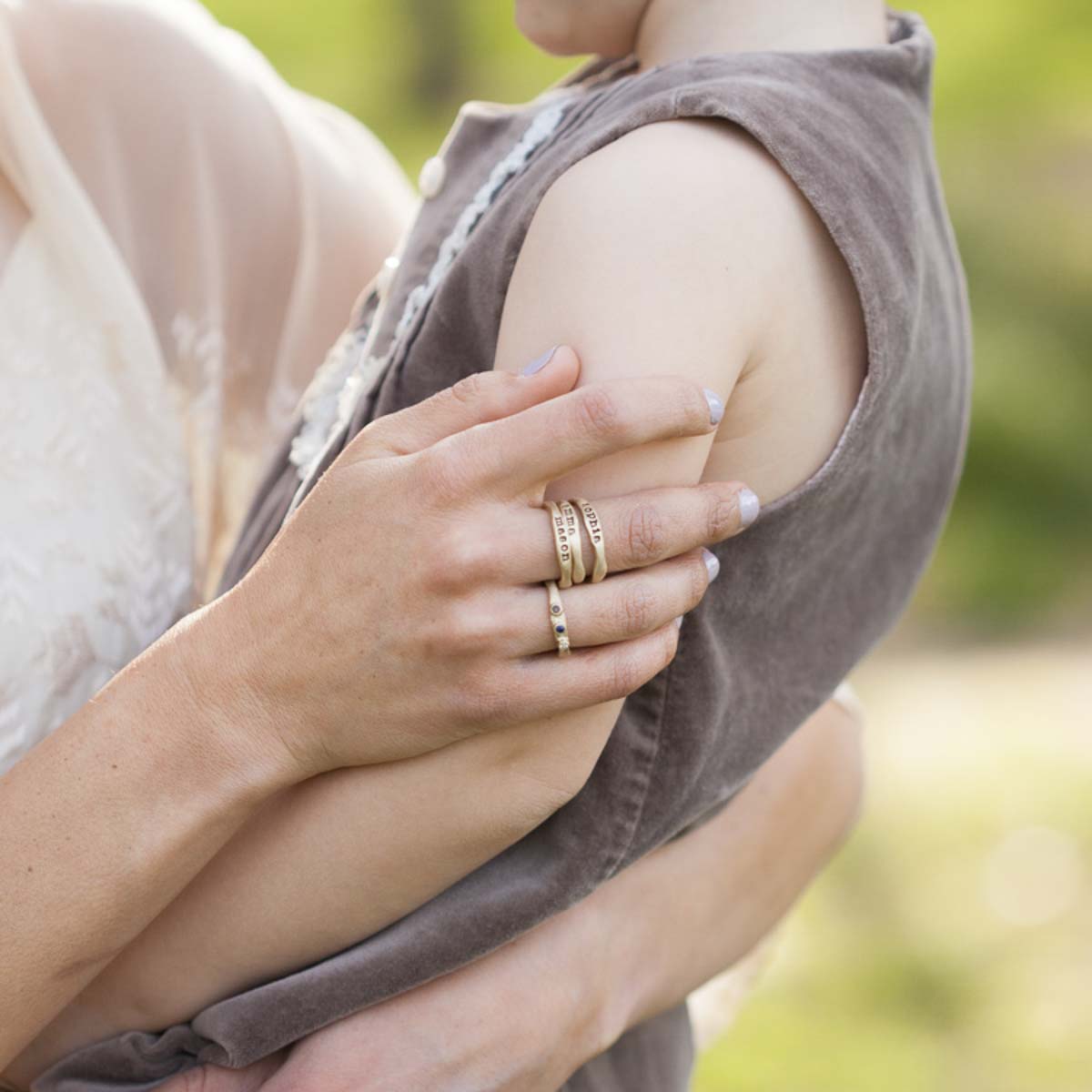 Woman showing her Personalized 10k yellow gold stackable name rings while holding her son