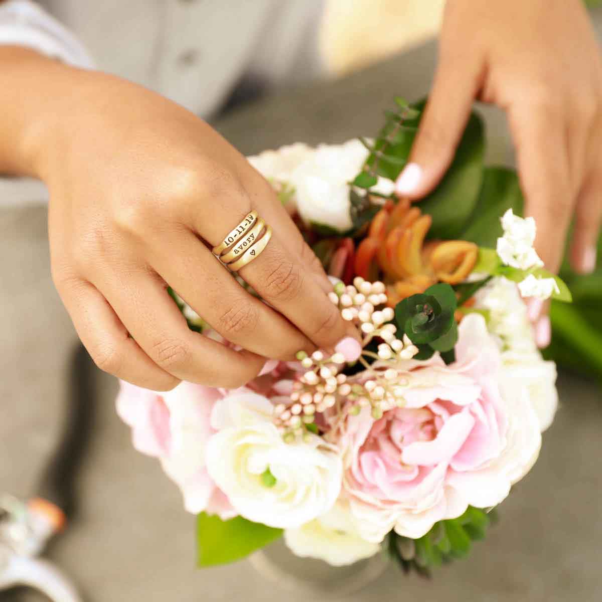 Woman wearing her Personalized 14k yellow gold stackable name rings while picking at flowers