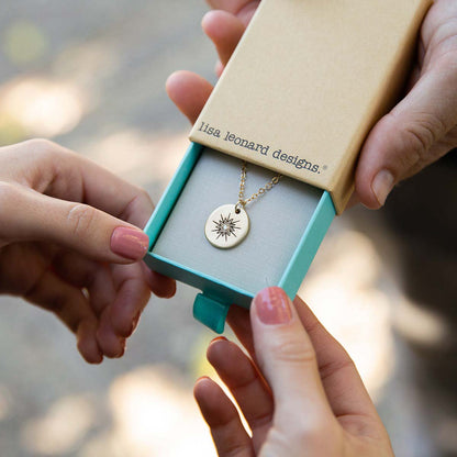 girl holding 10k yellow gold sunburst diamond necklace in a lisa leonard box