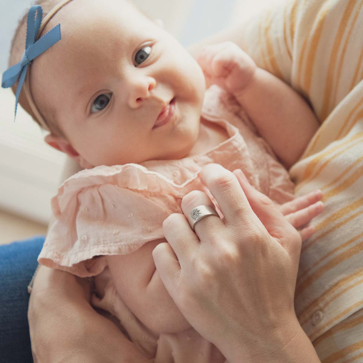 woman wearing her sterling silver sunburst diamond ring with a 3mm conflict free diamond while holding her baby