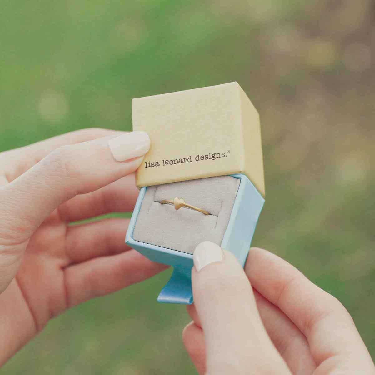 girl holding a 14k yellow gold sweet love ring - one heart in a lisa leonard box