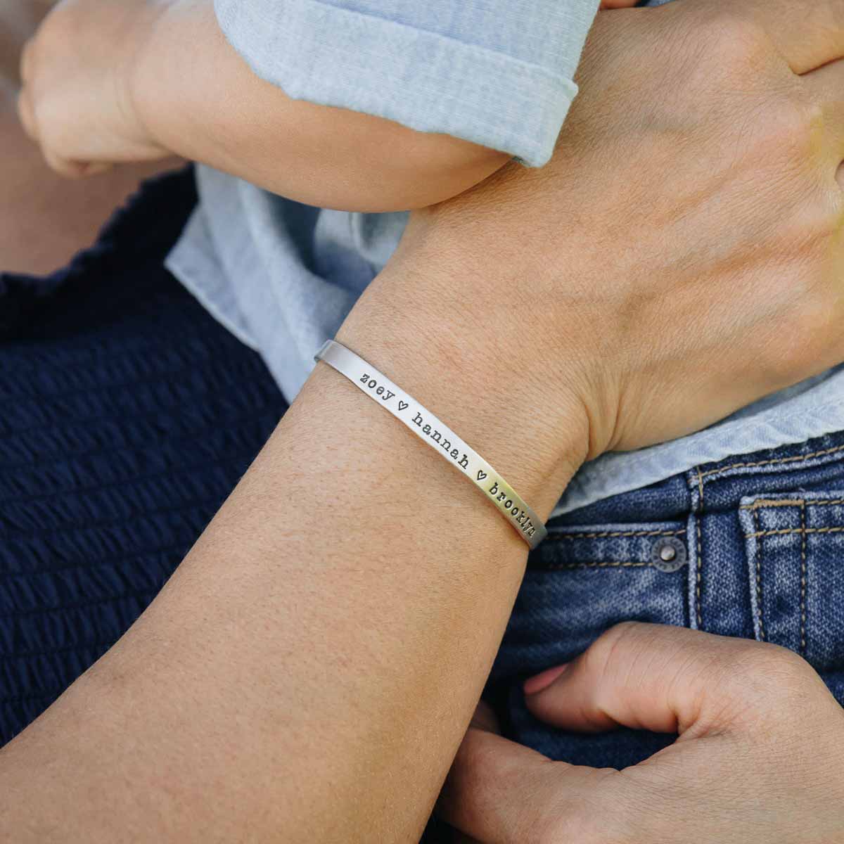 Woman holding child while showing her personalized sterling silver cuff bracelet