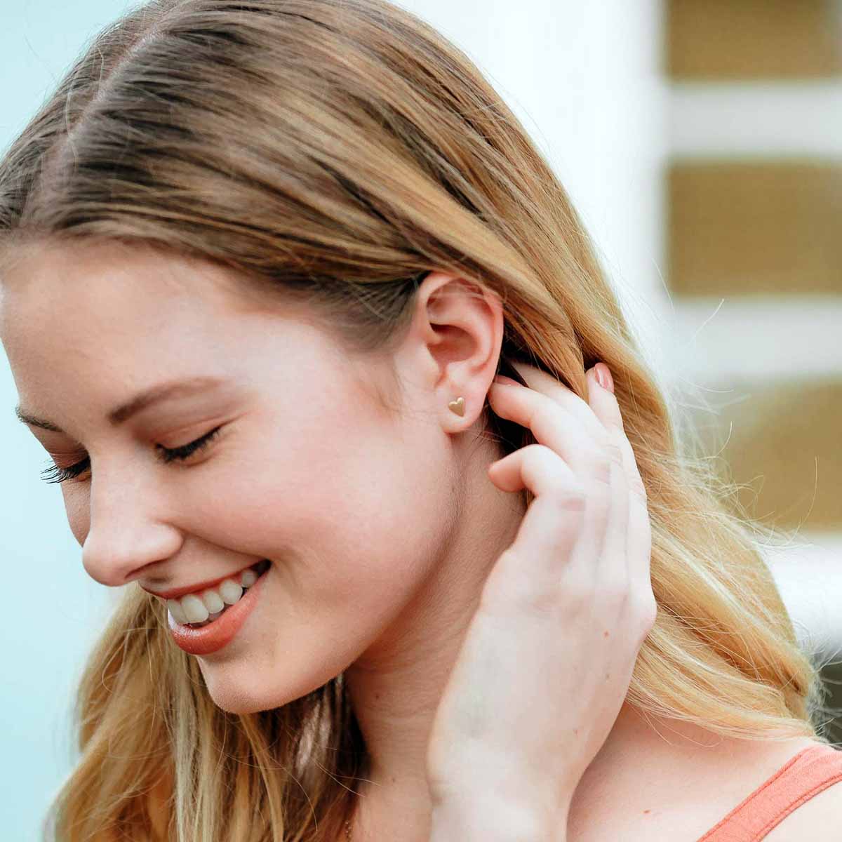 girl wearing 10k yellow gold tiny heart stud earrings with a matte brushed finish