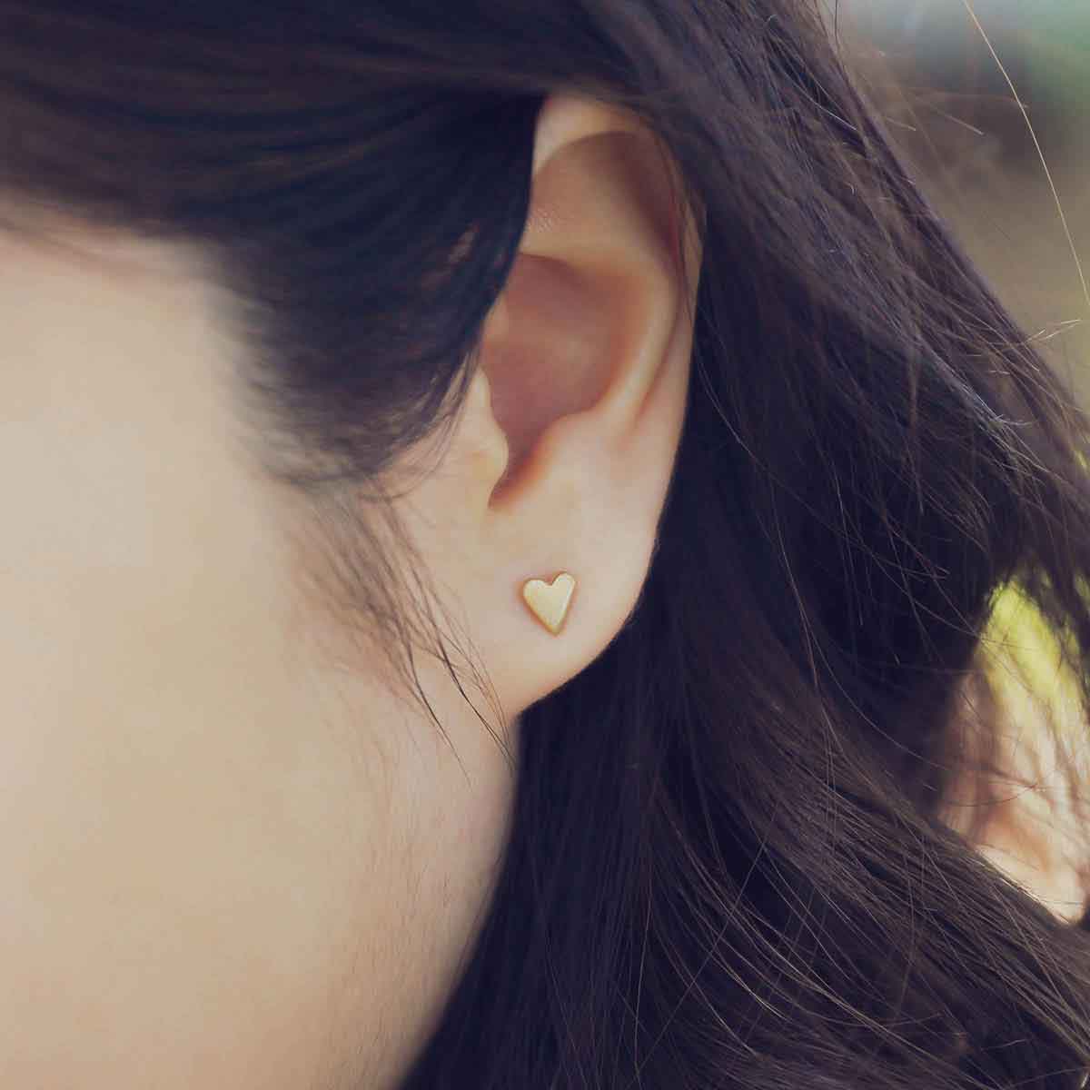 girl wearing 14k yellow gold tiny heart stud earrings with a matte brushed finish