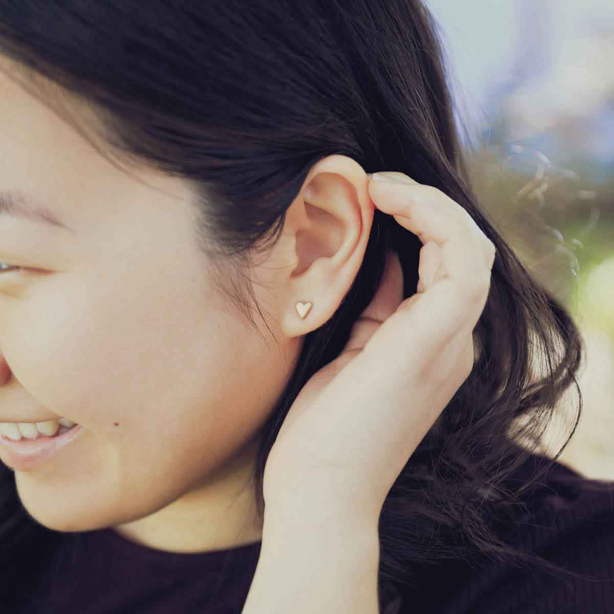 girl wearing 14k yellow gold tiny heart stud earrings with a matte brushed finish