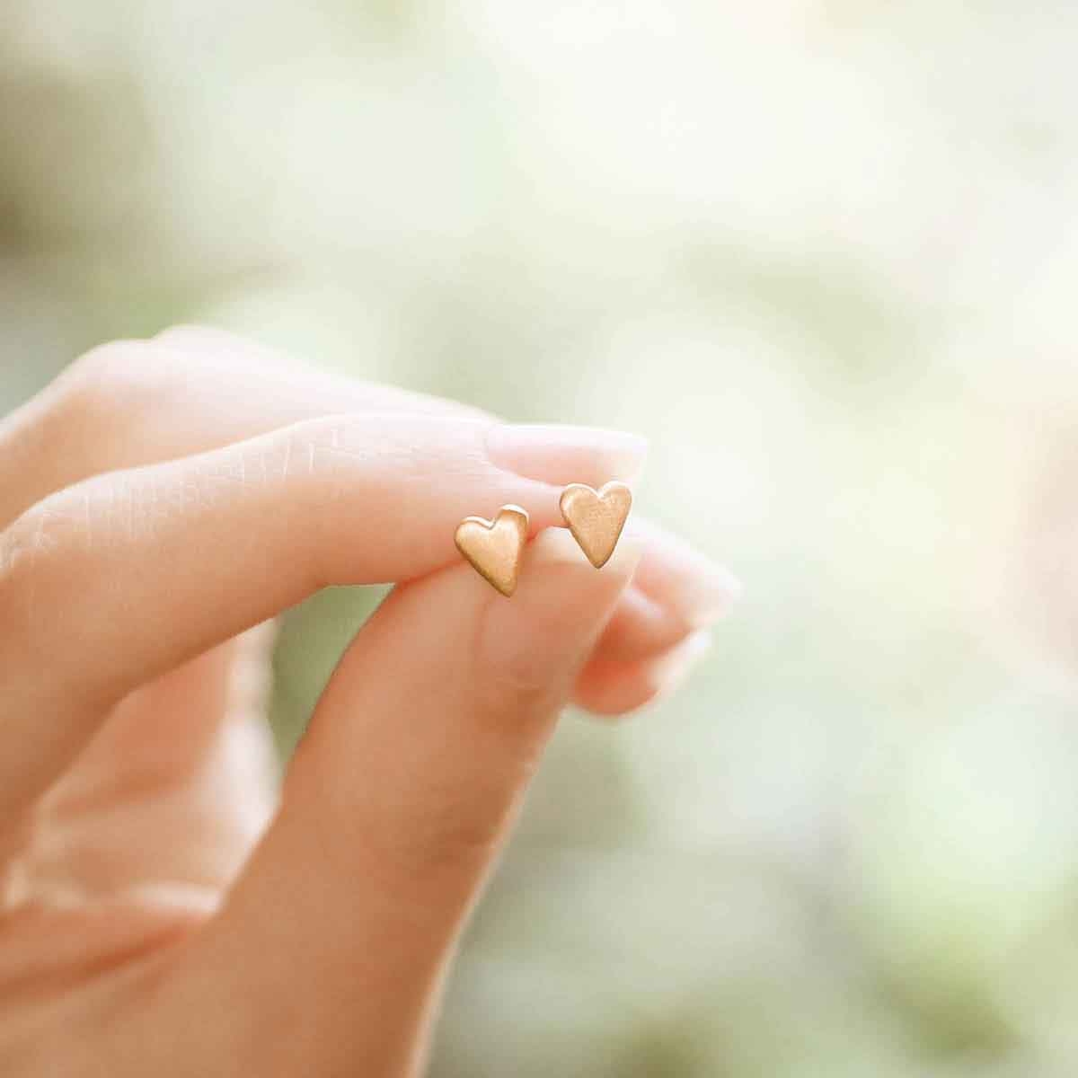 girl holding 10k yellow gold tiny heart stud earrings