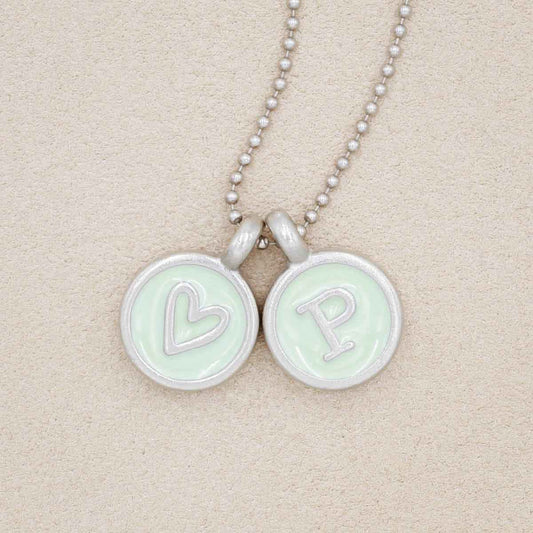 typewriter initial pewter necklace filled with light green epoxy, on a beige background