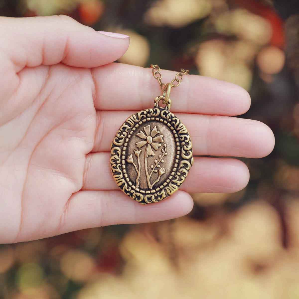 girl holding a gold plated vintage cameo necklace engraved with flowers 