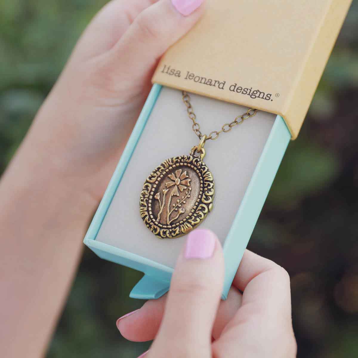 girl holding a gold plated vintage cameo necklace in a lisa leonard necklace box