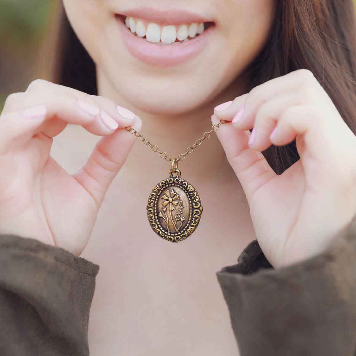 girl holding a gold plated vintage cameo necklace engraved with flowers 