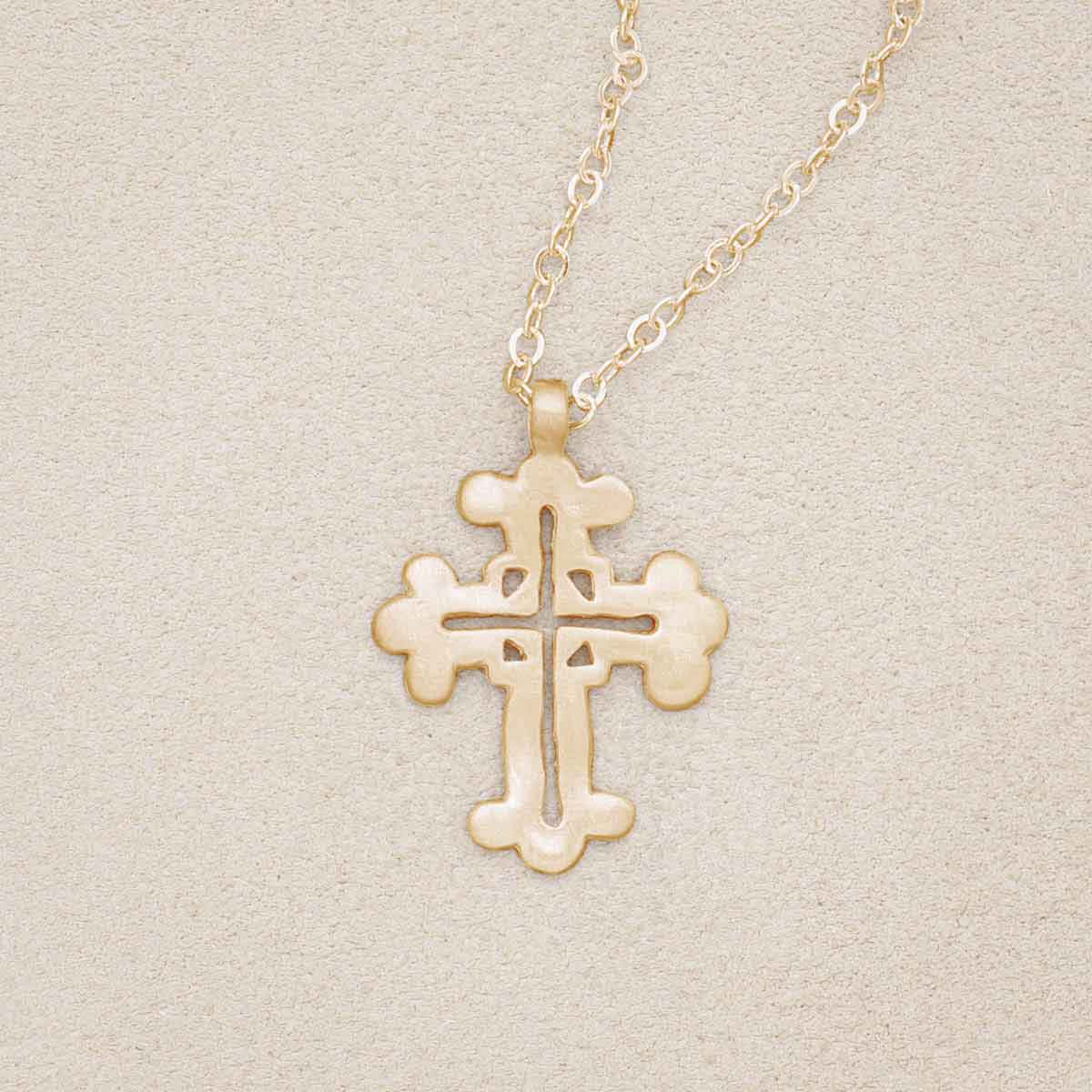 10k yellow gold work of art cross necklace, on beige background