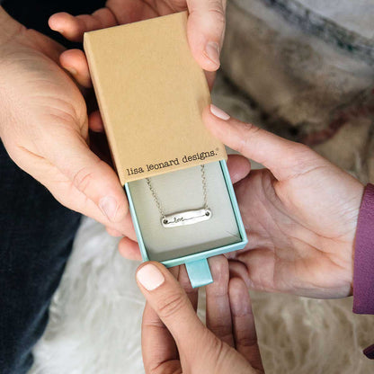 hands holding sterling silver written with love necklace in a lisa leonard box