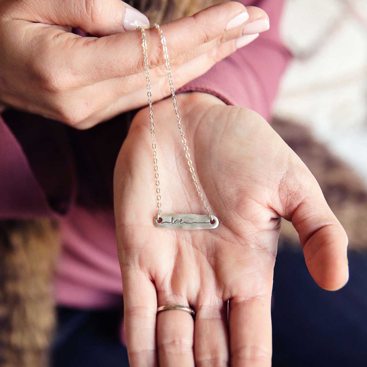 hand holding sterling silver written with love necklace