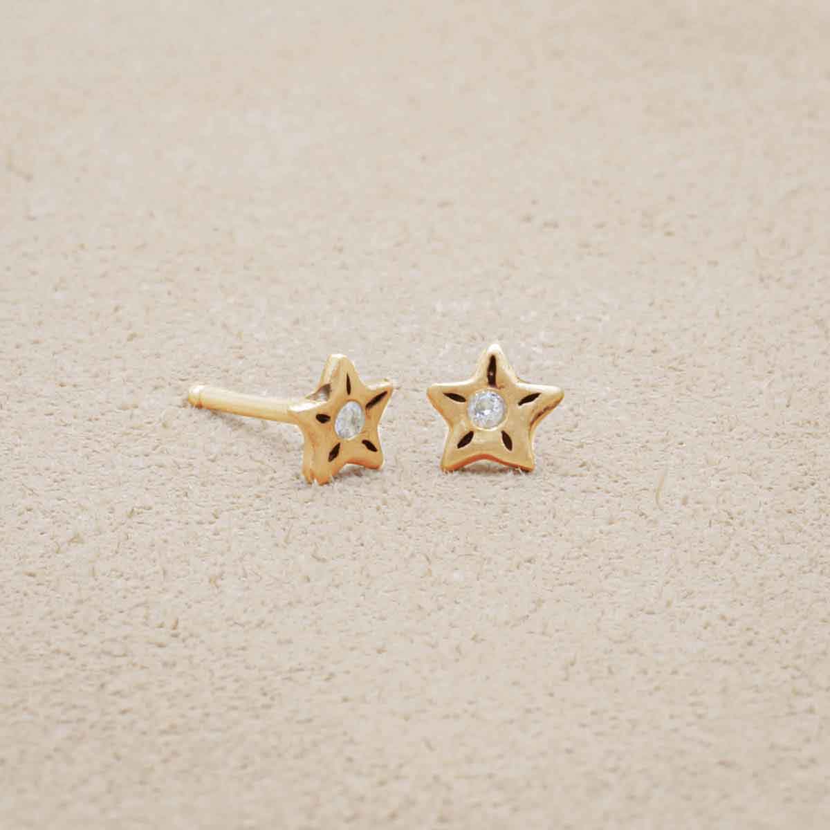 Your Spark Earrings, handcrafted in 14k yellow gold, set with a 1.5mm cubic zirconia, on beige background